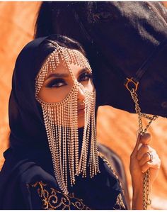 a woman wearing a headdress standing next to a horse with chains on it's face