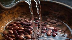 beans being poured into a wooden bowl filled with water