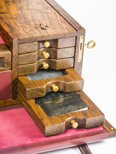 a wooden desk with three drawers and two cards in the bottom drawer, on top of a pink velvet covered surface