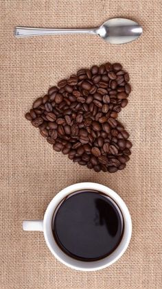 a cup of coffee next to a spoon and beans