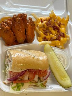 a lunch box with chicken wings, coleslaw, salad and pickle on it