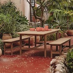 a wooden table with two benches in front of potted plants on the ground and words west elm above it