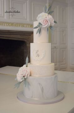 a three tiered wedding cake with flowers on the top and initials on the side