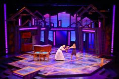 two women in white dresses on stage with purple lighting behind them and an open floor plan