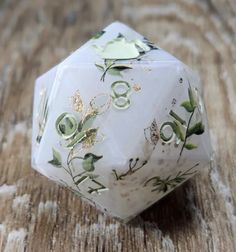 a close up of a white dice on a wooden surface with flowers and leaves painted on it