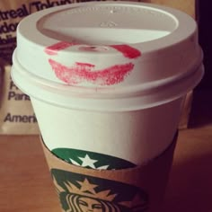 a starbucks cup with red lipstick drawn on the lid and bottom, sitting on a table