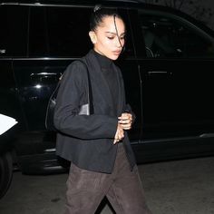 a woman in black jacket and pants walking past a car