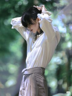 a woman in a white shirt and brown skirt holding her hands to her head while standing next to trees