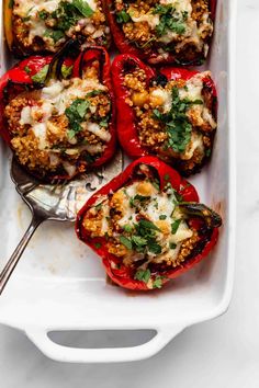 stuffed red peppers in a white casserole dish with a spoon and serving utensils