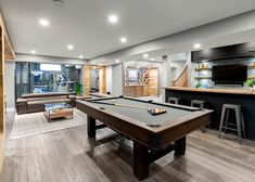 a pool table in the middle of a living room with an entertainment center and bar