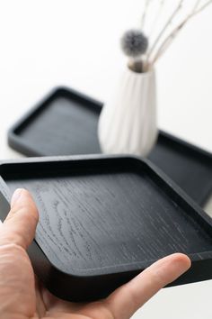 a hand is holding a black tray on a table