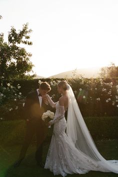 a bride and groom standing in front of some white flowers at their wedding day with the sun shining on them