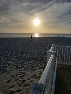 the sun is setting over the beach with people walking on it