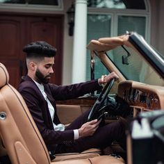 a man sitting in the driver's seat of a car with his hand on the steering wheel