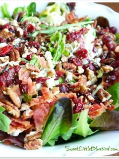 a salad with bacon, lettuce and cranberries in it on a white plate