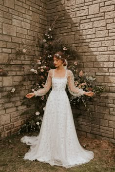 a woman standing in front of a brick wall wearing a wedding dress with long sleeves