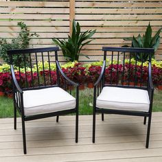 two black chairs sitting on top of a wooden deck next to flowers and plants in the background