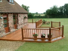 a wooden deck in front of a brick building with potted plants on the ground