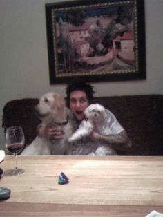 a man sitting at a table with two dogs and a glass of wine in front of him