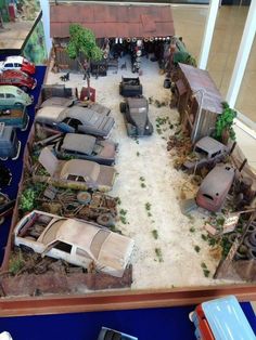 an assortment of old model cars on display in a building with lots of dirt and grass