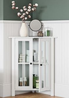 a white cabinet sitting next to a toilet in a room with green walls and wooden floors