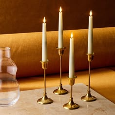 three candles on a table next to a vase with water in it and another candle holder