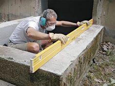 a man in white shirt and safety goggles working on cement structure with measuring tape