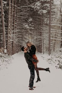 a man holding a woman in the snow with trees behind him and all around them