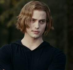 a young man with long hair wearing a black hoodie and looking at the camera