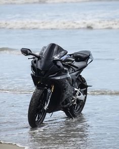 a black motorcycle parked on the beach next to the ocean water with waves coming in