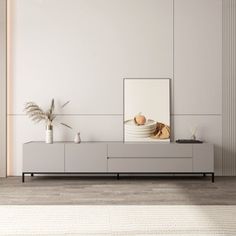 a living room with white walls and wooden flooring is pictured in this image, there are plants on the sideboard