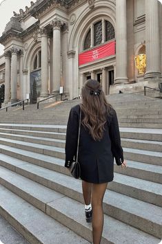 a woman walking down some steps in front of a building with columns and arches on it