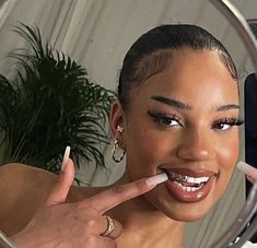 a close up of a person brushing her teeth in front of a mirror with a plant