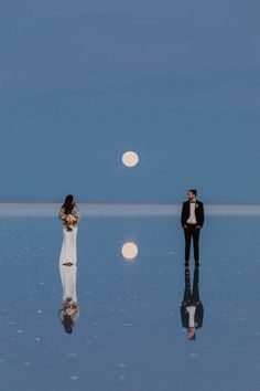 a man and woman are standing in the middle of an empty salt flat with full moon behind them