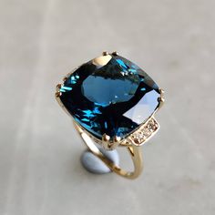 This stunning ring is set in 14k Solid Yellow Gold with Natural London Blue Topaz and Diamond with utmost precision. It is an unique statement gemstone ring for nearly every occasion and is completely hassle-free jewelry. ITEM DETAILS * CENTER GEM: London Blue topaz * GEM SIZE: 15X15mm * GEM SHAPE: Cushion * Gem weight: 15.95 carats * SIDE GEM: Diamond * GEM SIZE: 1.50mm (6 pcs),  * GEM SHAPE: ROUND * Gem weight: 0.083 carats * Total Gem weight: 16.03 carats * Gold Purity: 14KT * Gold Weight: 3.58 gram * Total Weight of the Ring: 6.79 gram The Gold purity is guaranteed and it comes with authentic 14KT gold hallmark. Since my items are handmade, they are absolutely nickel and lead free. CUSTOMIZATION: * Size Customization is available for this ring and it is available in all ring sizes. Kin Luxury Gold Topaz Ring With Gemstone Accents, Luxury Vintage Topaz Ring As A Gift, Big Gem Ring, Luxury Timeless Gold Topaz Ring, Classic Luxury Topaz Ring With Polished Finish, Yellow Topaz Ring Designs, Blue Cushion Cut Ring With Gemstone Accents, London Blue Topaz Jewelry, Blue Topaz Jewelry