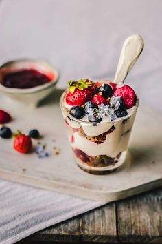 a dessert with berries and yogurt in a glass on a tray next to some fruit