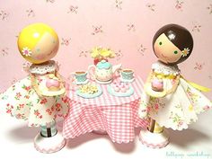 two figurines are sitting at a table with tea cups and plates on it