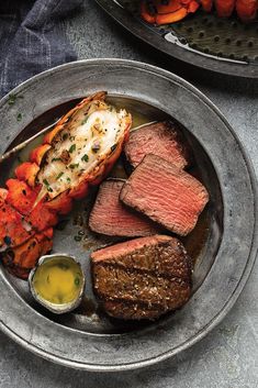 a plate with steak, carrots and other food on it next to a bowl of dipping sauce