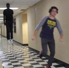 two people walking down a hallway with one person wearing headphones and the other has an arrow on his forehead