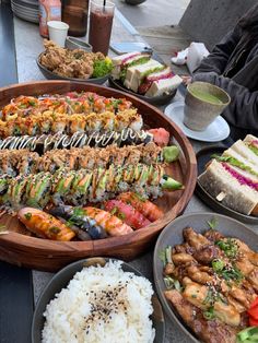 an assortment of sushi and other food items on a wooden platter with people sitting at a table