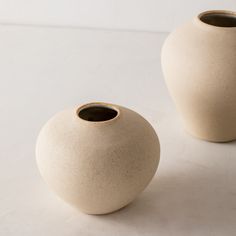 two white vases sitting next to each other on top of a table with no one in them