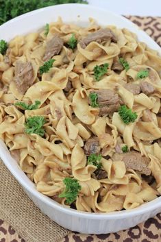 a white bowl filled with pasta and meat covered in broccoli on top of a table