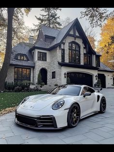 a white sports car parked in front of a large house with trees and bushes around it