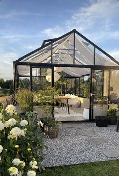 a glass house sitting on top of a lush green field next to flowers and trees