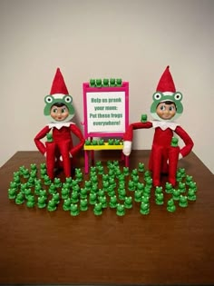 two elfs are standing in front of a sign with green buttons on it and one is pointing at the board