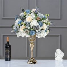 a vase filled with white and blue flowers next to a bottle of wine on a table