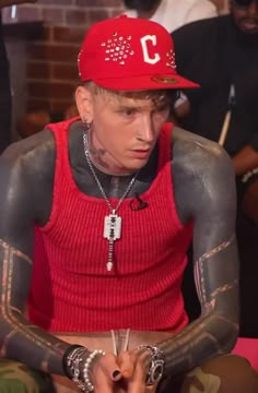 a man with tattoos on his arm and wearing a red hat