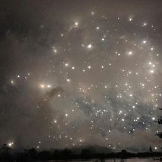 fireworks are lit up in the night sky over a body of water with trees on either side