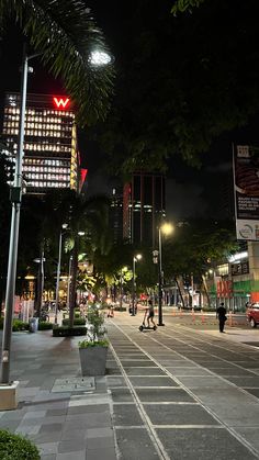 a city street at night with people walking and riding skateboards on the sidewalk near tall buildings