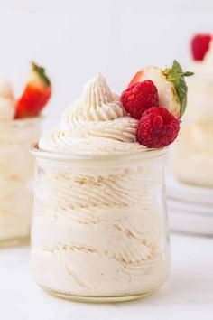 a jar filled with whipped cream and topped with raspberries next to another jar full of strawberries